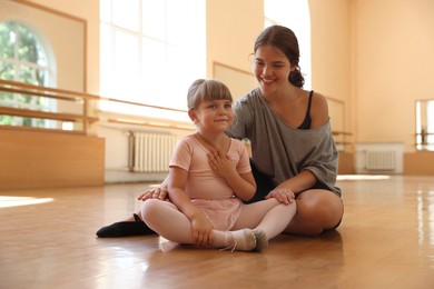 Photo of Happy ballet teacher working with little girl on floor in dance class
