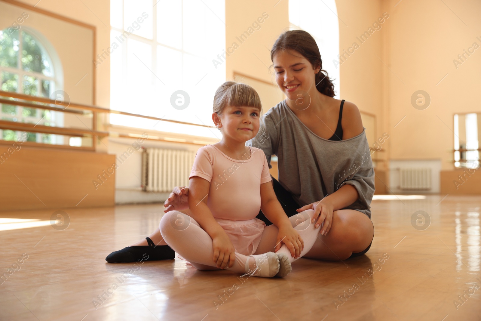 Happy ballet teacher working with little girl on floor in dance class Photo of Happy ballet teacher working with little girl on floor in dance class