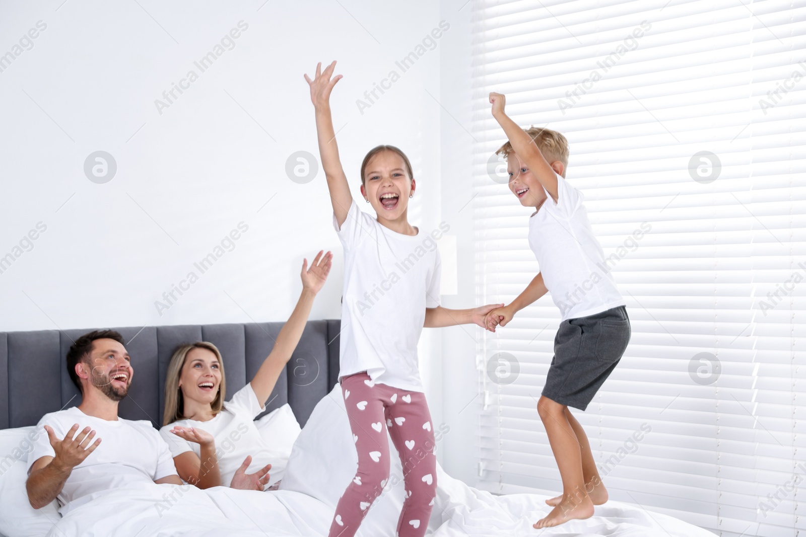 Photo of Happy parents lying in bed while their children jumping at home. Family