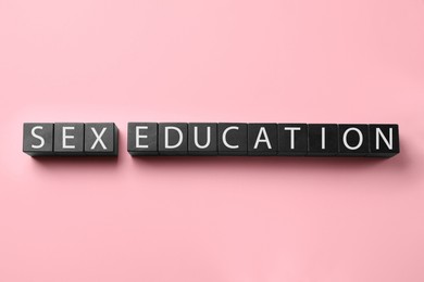 Photo of Words Sex Education made with black cubes on pink background, flat lay