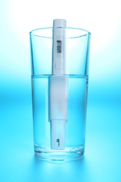 Photo of Nitrate tester in glass of water on light blue background, closeup