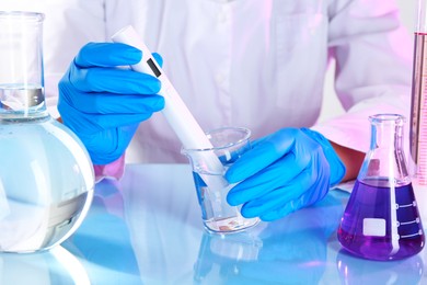 Photo of Scientist examining water with nitrate tester at white table in laboratory, closeup