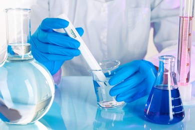 Photo of Scientist examining water with nitrate tester at white table in laboratory, closeup