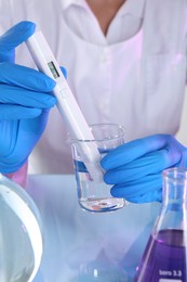 Photo of Scientist examining water with nitrate tester at white table in laboratory, closeup