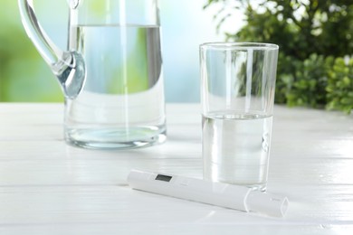 Photo of Nitrate tester and glass of water on white wooden table, closeup