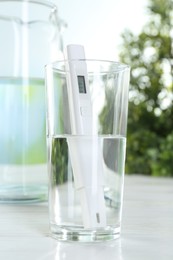 Photo of Nitrate tester in glass of water on white wooden table, closeup