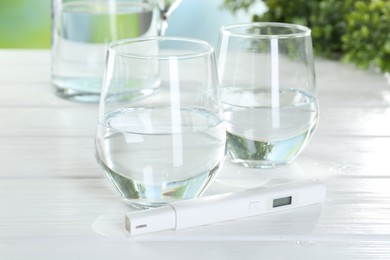 Photo of Nitrate tester and glasses of water on white wooden table, closeup