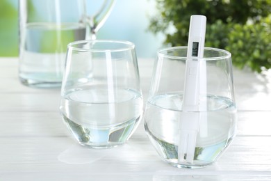 Photo of Nitrate tester in glass of water on white wooden table, closeup