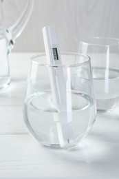 Photo of Nitrate tester in glass of water on white wooden table, closeup