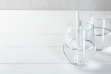 Photo of Nitrate tester in glass of water on white wooden table, closeup. Space for text