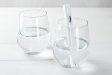 Photo of Nitrate tester in glass of water on white wooden table, closeup