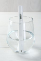 Photo of Nitrate tester in glass of water on white wooden table, closeup