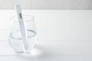 Photo of Nitrate tester in glass of water on white wooden table, closeup. Space for text