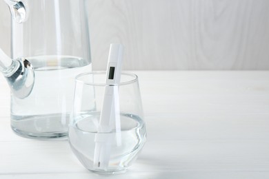 Photo of Nitrate tester in glass of water on white wooden table, closeup. Space for text