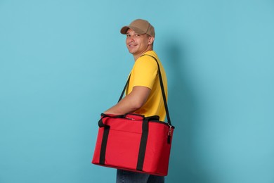Photo of Courier with thermo bag on light blue background. Food delivery service