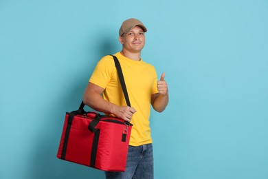 Photo of Courier with thermo bag showing thumbs up on light blue background. Food delivery service
