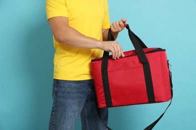 Photo of Courier with thermo bag on light blue background, closeup. Food delivery service