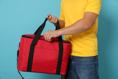 Photo of Courier with thermo bag on light blue background, closeup. Food delivery service
