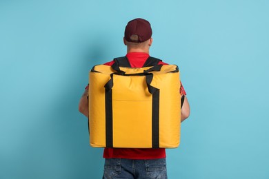 Photo of Courier with thermo bag on light blue background, back view. Food delivery service