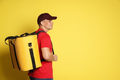 Photo of Courier with thermo bag on yellow background, space for text. Food delivery service