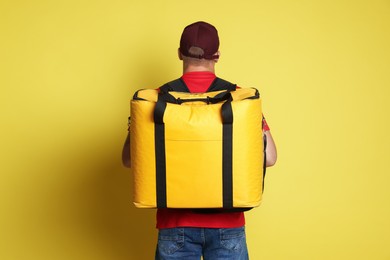 Photo of Courier with thermo bag on yellow background, back view. Food delivery service