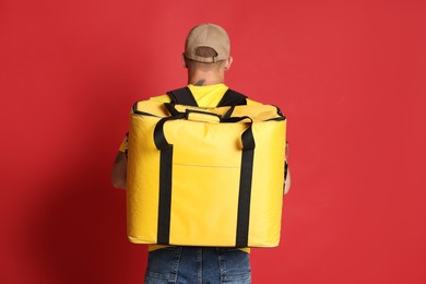 Photo of Courier with thermo bag on red background, back view. Food delivery service