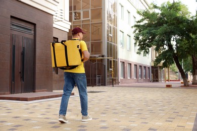 Photo of Courier with thermo bag on city street, back view. Food delivery service
