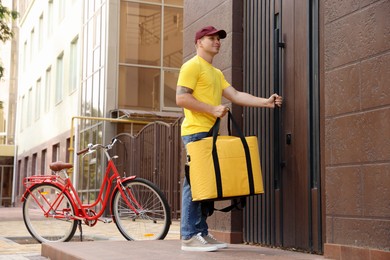 Photo of Courier with thermo bag near building outdoors. Food delivery service