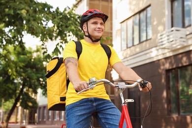 Photo of Courier with thermo bag riding bicycle outdoors, low angle view. Food delivery service
