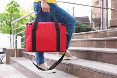 Photo of Courier with thermo bag on stairs outdoors, closeup. Food delivery service