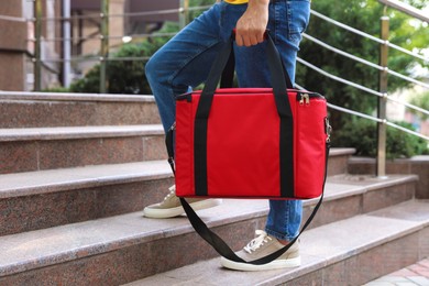 Photo of Courier with thermo bag on stairs outdoors, closeup. Food delivery service