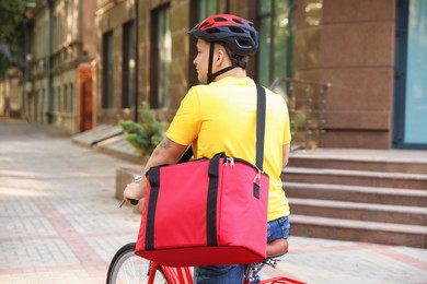 Photo of Courier with thermo bag riding bicycle outdoors. Food delivery service