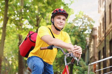 Photo of Courier with thermo bag on bicycle outdoors, low angle view. Food delivery service