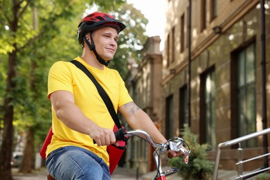Photo of Courier with thermo bag riding bicycle outdoors, low angle view. Food delivery service
