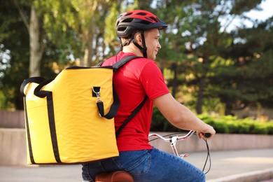 Photo of Courier with thermo bag riding bicycle outdoors. Food delivery service