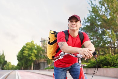 Photo of Courier with thermo bag on bicycle outdoors, space for text. Food delivery service