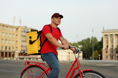 Photo of Courier with thermo bag riding bicycle outdoors. Food delivery service