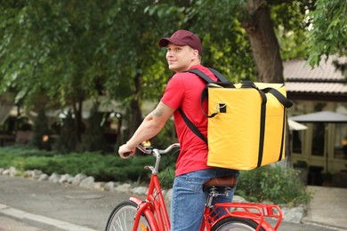 Photo of Courier with thermo bag riding bicycle outdoors, space for text. Food delivery service