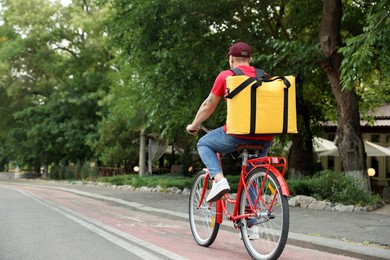Photo of Courier with thermo bag riding bicycle outdoors, back view. Food delivery service