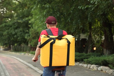 Photo of Courier with thermo bag riding bicycle outdoors, back view. Food delivery service