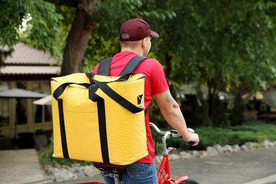 Photo of Courier with thermo bag riding bicycle outdoors, space for text. Food delivery service