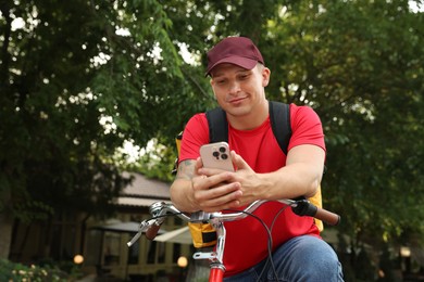 Photo of Courier with thermo bag and smartphone on bicycle outdoors, space for text. Food delivery service
