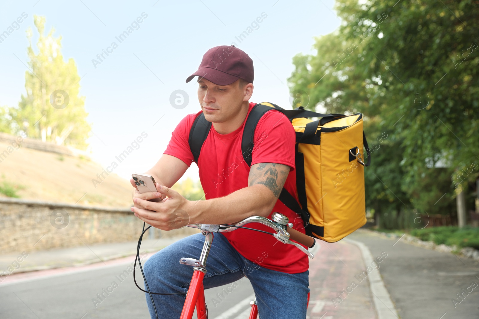Courier with thermo bag and smartphone on bicycle outdoors. Food delivery service Photo of Courier with thermo bag and smartphone on bicycle outdoors. Food delivery service