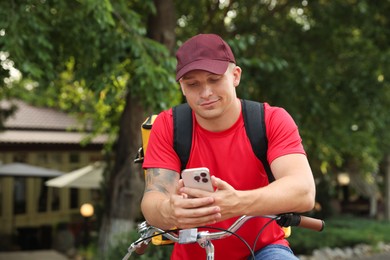 Photo of Courier with thermo bag and smartphone on bicycle outdoors. Food delivery service
