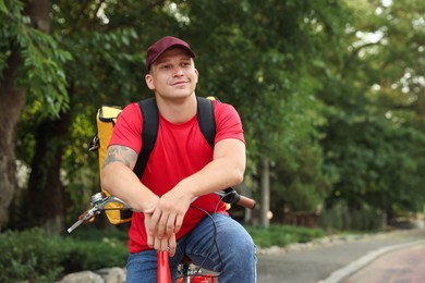 Photo of Courier with thermo bag on bicycle outdoors, space for text. Food delivery service