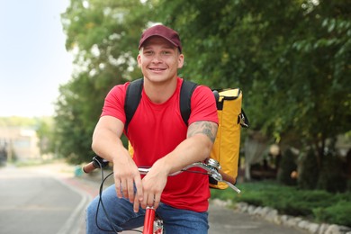 Photo of Courier with thermo bag on bicycle outdoors. Food delivery service