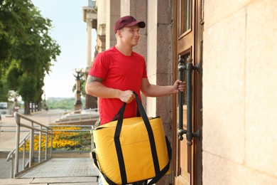 Photo of Courier with thermo bag near door outdoors. Food delivery service