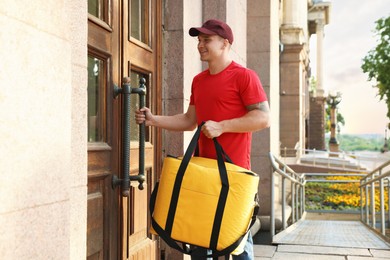 Photo of Courier with thermo bag near door outdoors. Food delivery service