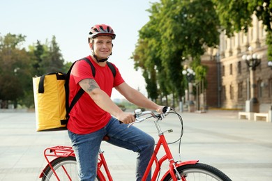 Photo of Courier with thermo bag on bicycle outdoors. Food delivery service