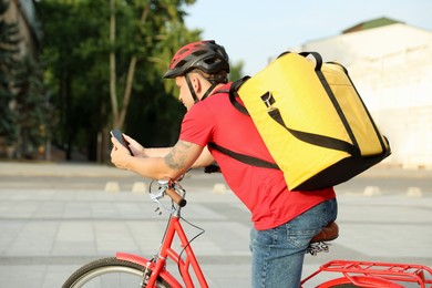 Photo of Courier with thermo bag and smartphone on bicycle outdoors. Food delivery service